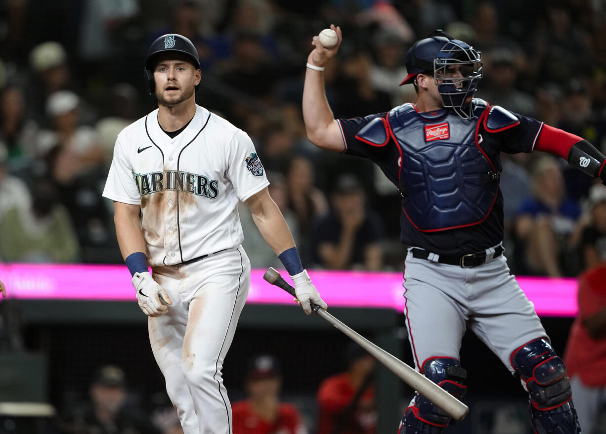 Seattle Mariners' Jarred Kelenic walks away after striking out, while Washington Nationals catcher Riley Adams throws the ball back during the 11th inning of a baseball game Tuesday, June 27, 2023, in Seattle. The Nationals won 7-4.