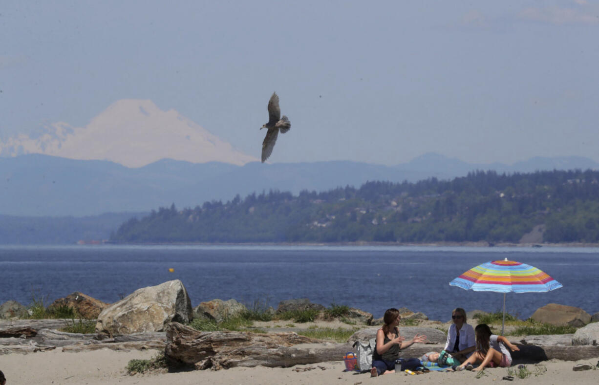 People sit outside on a warm spring day as Mount Baker rises in the distance, in Edmonds, Wash., Saturday, May 13, 2023.