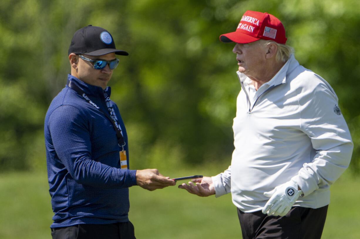 Walt Nauta, left, takes a phone from Former President Donald Trump during the LIV Golf Pro-Am at Trump National Golf Club, Thursday, May 25, 2023, in Sterling, Va. When Trump appears in federal court in Miami, he will likely be joined on the witness stand by a man well-practiced in standing by his side: auta, his valet turned co-conspirator.