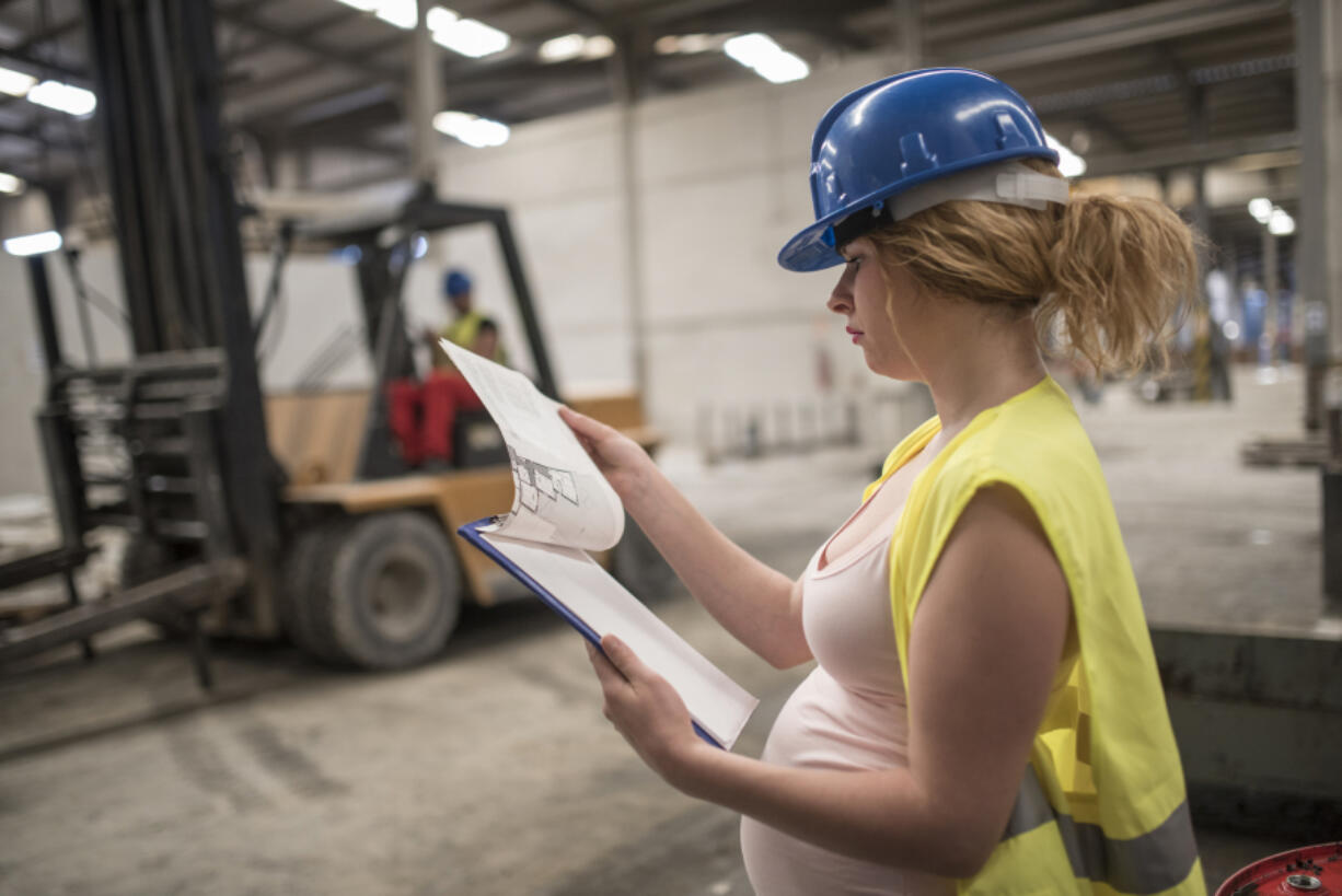 Pregnant woman working and forklift in bakcground