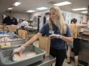 Volunteers Leslie Matheney, center, and Vitaliy Shkurov, left, of IDM Cos. help assemble lunches for kids in need while working in the kitchen at Fort Vancouver High School. Share is celebrating the 20th anniversary of its summer meal program.