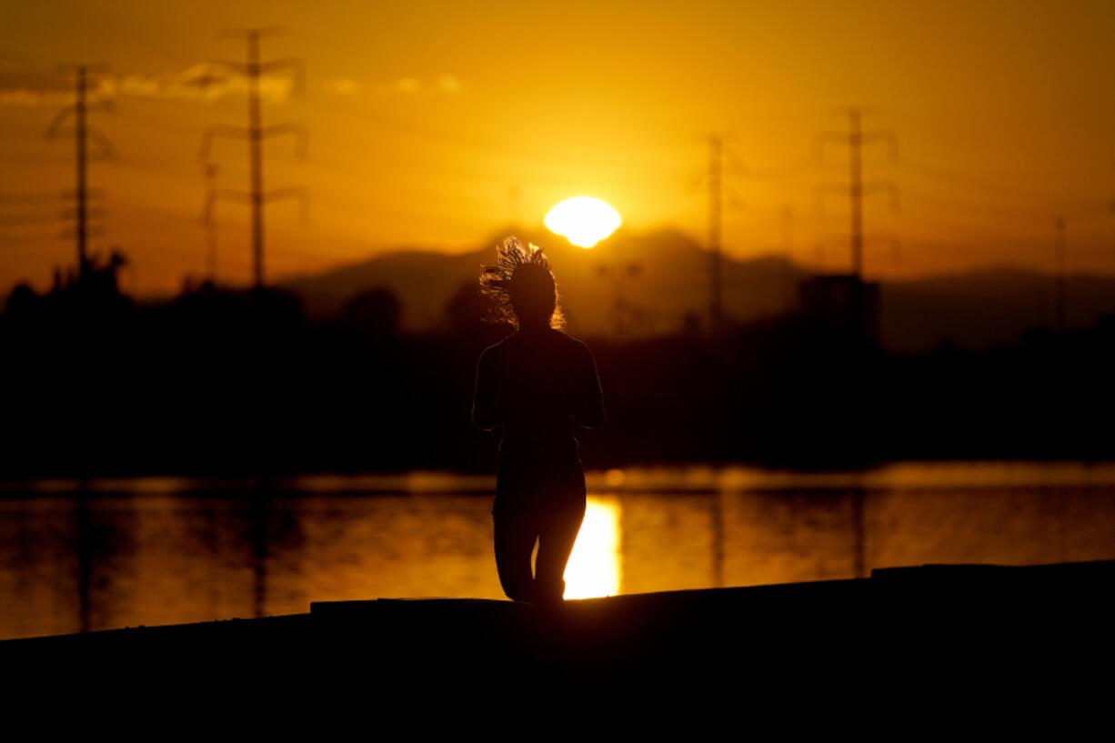 FILE - A runner jogs along Tempe Town Lake at sunrise,  July 12, 2023 in Tempe, Ariz. President Joe Biden plans to announce new steps to address the extreme heat that has threatened millions of Americans, most recently in the Southwest.