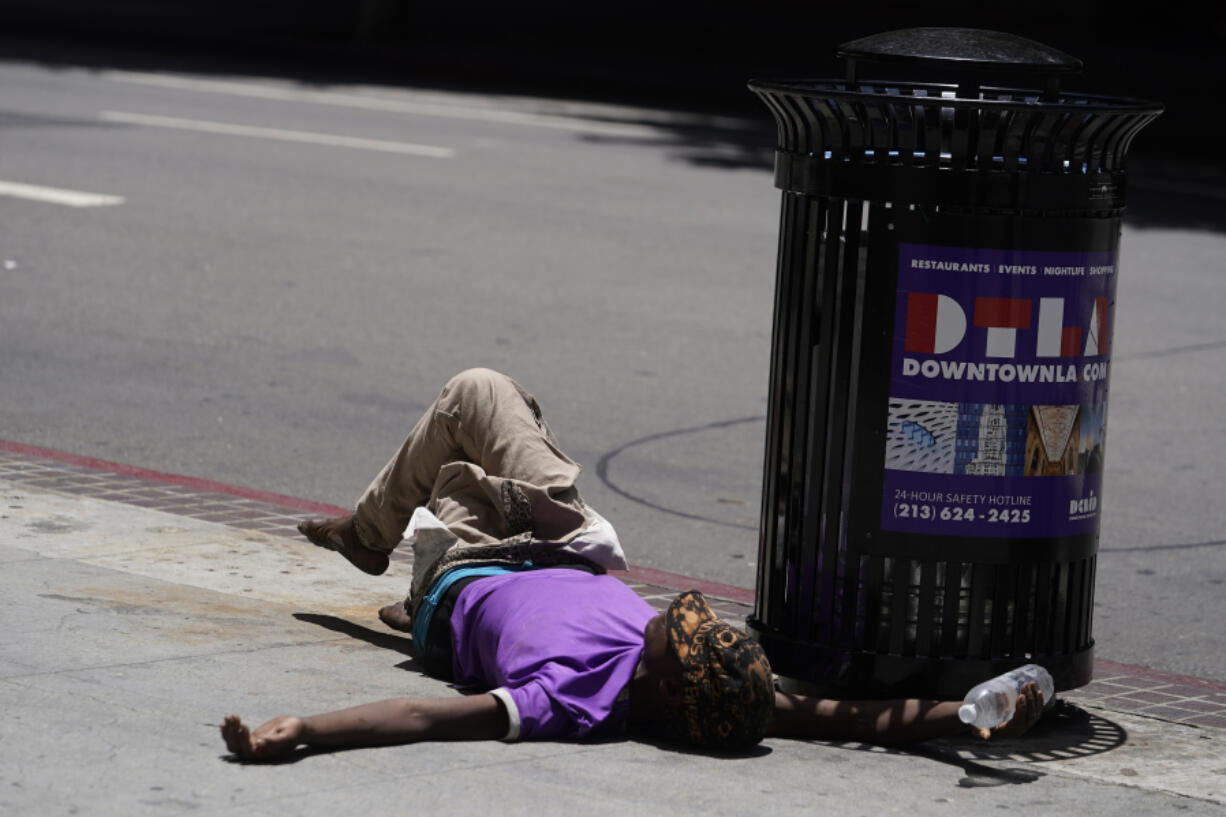 FILE - A homeless person lies on the sidewalk while holding a water bottle, Sunday, July 2, 2023, in downtown Los Angeles. Excessive heat warnings remain in place in many areas across the U.S. and are expected to last at least through Monday.