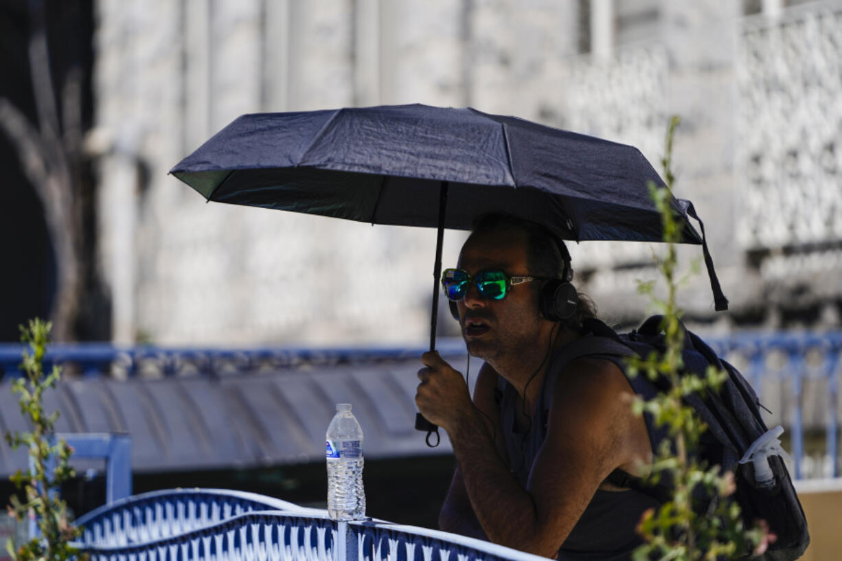 A man uses an umbrella to avoid the midday sun, Tuesday, July 11, 2023, in Los Angeles. Southern California is expecting high temperatures between 100 to 110 degrees Fahrenheit later this week according to the National Weather Service.