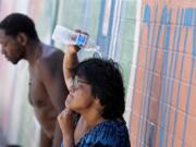 FILE - People, who are homeless, try to cool down with chilled water outside the Justa Center, a day center for homeless people 55 years and older, July 14, 2023, in downtown Phoenix. Homeless people are among the people most likely to die in the extreme heat in Phoenix.