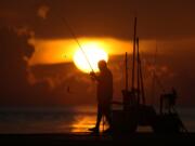 FILE - A fisherman reels in his catch as the sun rises over the Atlantic Ocean, June 28, 2023, in Bal Harbour, Fla. An already warming Earth steamed to its hottest June on record, with global oceans setting temperature records for the third straight month, the U.S. National Oceanic and Atmospheric Administration announced Thursday, July 13.