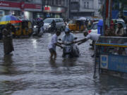 A traffic police officer, right and a man, left help a motorist at a water logged street during rain in Hyderabad, India, Thursday, July 20, 2023. India receives its monsoon rains from June to October.