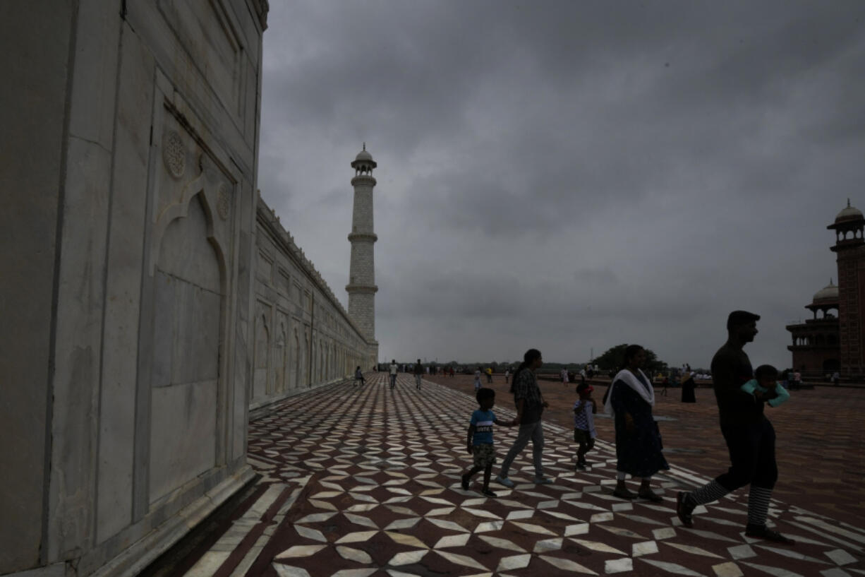 A family walks around the Taj Mahal as monsoon clouds gather over the Agra skyline, India, Saturday, July 8, 2023.