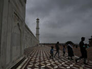 A family walks around the Taj Mahal as monsoon clouds gather over the Agra skyline, India, Saturday, July 8, 2023.