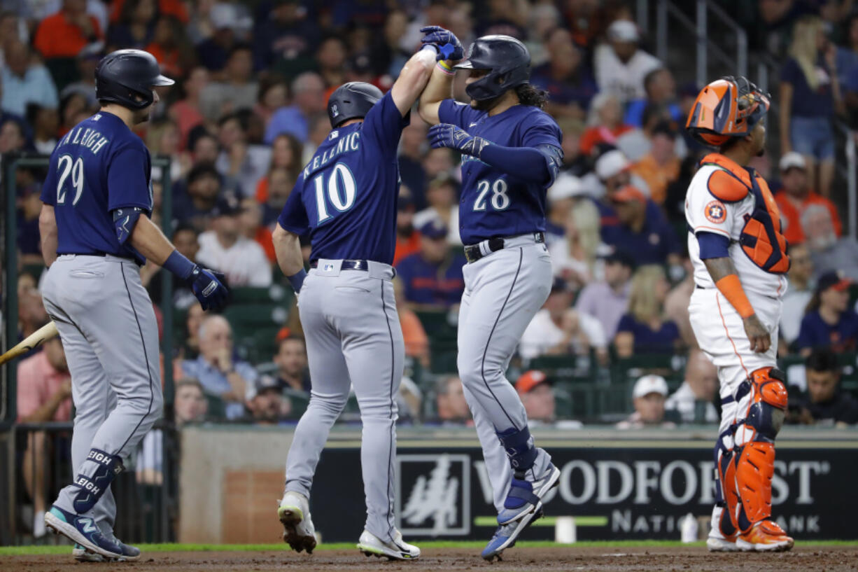 Seattle Mariners' Jarred Kelenic (10) and Eugenio Suarez (28) celebrate after they scored on a two-run home run by Suarez during the second inning of a baseball game Thursday, July 6, 2023, in Houston. Mariners' Cal Raleigh (29) and Houston Astros catcher Martin Maldonado, right, look on.