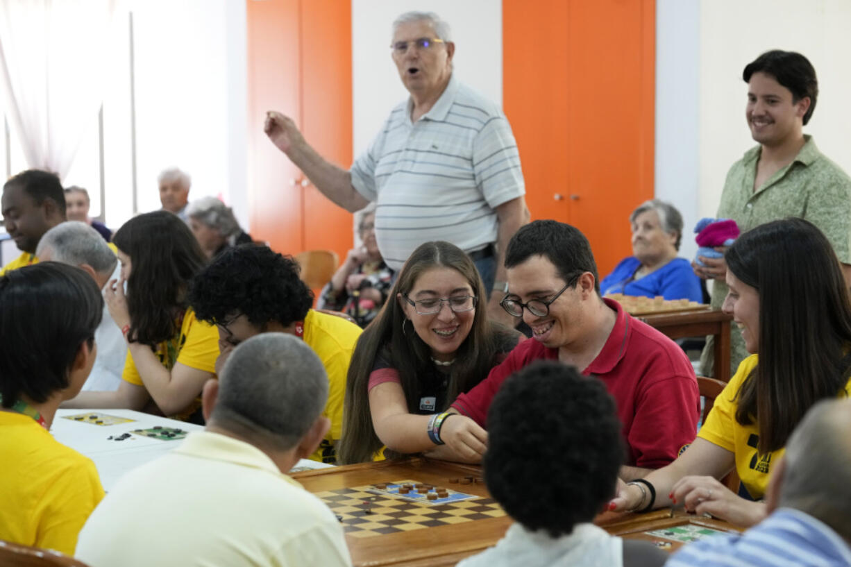 Father Crespo, in the background, calls the numbers while World Youth Day volunteers play bingo with residents of a parish center in Lisbon, Thursday, July 27, 2023. When Pope Francis attends the international World Youth Day in Lisbon he will pay a visit to the parish center that cares for hundreds of residents of the impoverished neighborhood of Serafina.