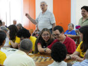 Father Crespo, in the background, calls the numbers while World Youth Day volunteers play bingo with residents of a parish center in Lisbon, Thursday, July 27, 2023. When Pope Francis attends the international World Youth Day in Lisbon he will pay a visit to the parish center that cares for hundreds of residents of the impoverished neighborhood of Serafina.