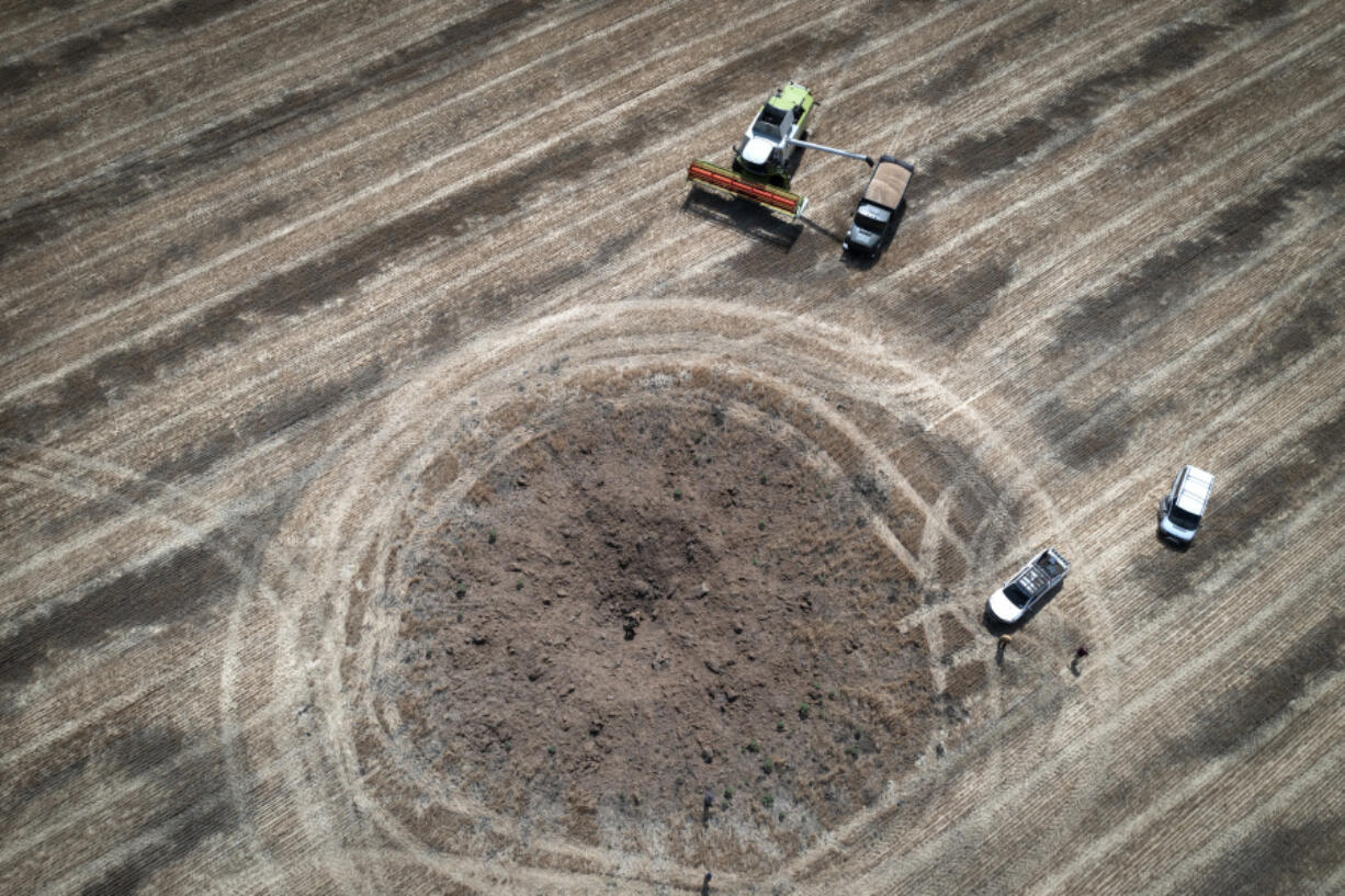 FILE - A farmer collects harvest in a field ten kilometers from the front line, around a crater left by a Russian rocket in the foreground, in the Dnipropetrovsk region, Ukraine, July 4, 2022. Agreements that the U.N. and Turkey brokered with Ukraine and Russia to allow food and fertilizer to get from the warring nations to parts of the world where millions are going hungry have eased concerns over global food security. But they face increasing risks. Moscow has ramped up its rhetoric, saying it may not extend the deal that expires Monday July 17, 2023, unless its demands are met.