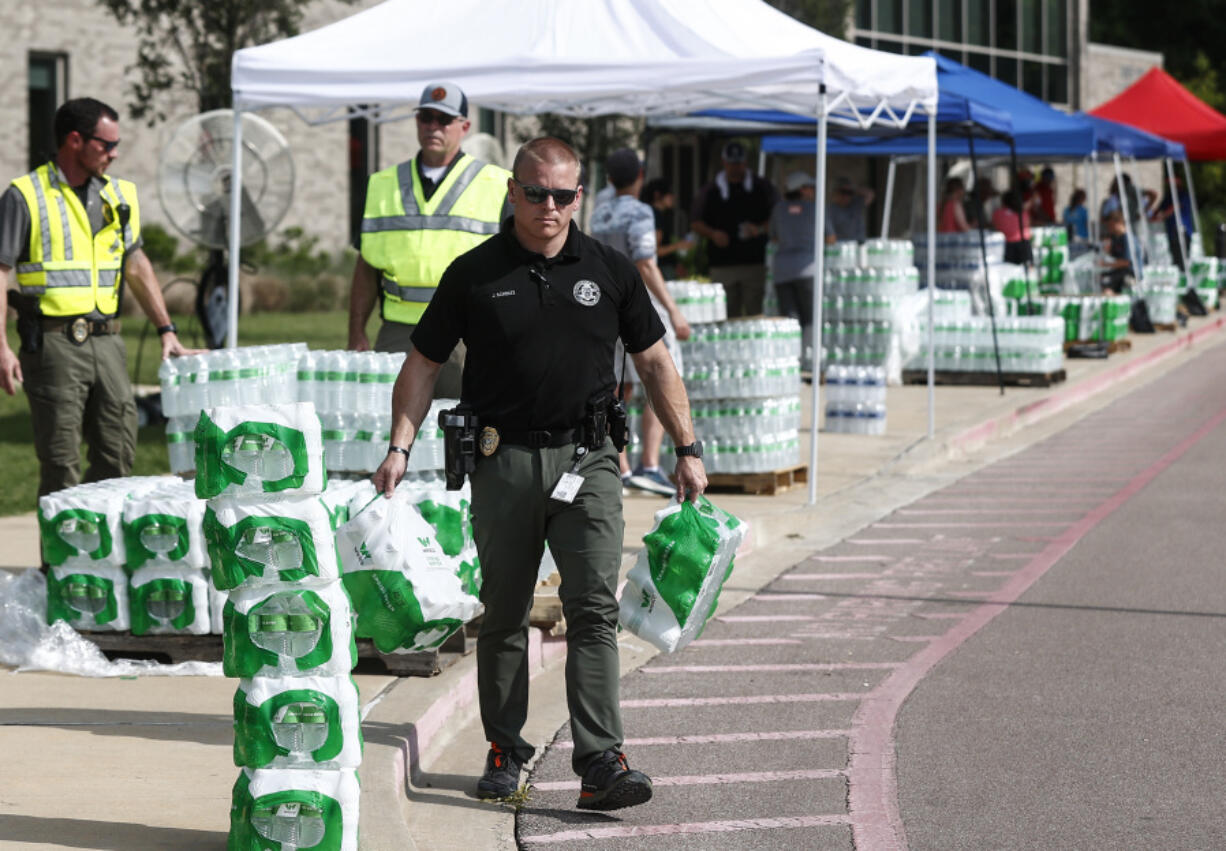 A police officer helps hand out bottled water to residents on Monday, July 24, 2023 at Forest Hill Elementary School in Germantown, Tenn. Residents of the Tennessee city were told that diesel fuel spilled into a local reservoir, and to avoid drinking tap water. People remain under an order Wednesday, July 26 to avoid using water for everything except flushing toilets. They can't drink or boil tap water, or use it showering or bathing.