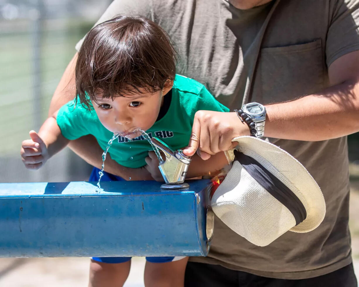 Abe Perez lifts his 2-year-old son Mavy, for a drink of water from a fountain at Lanark Park in Canoga Park on a hot summer afternoon.