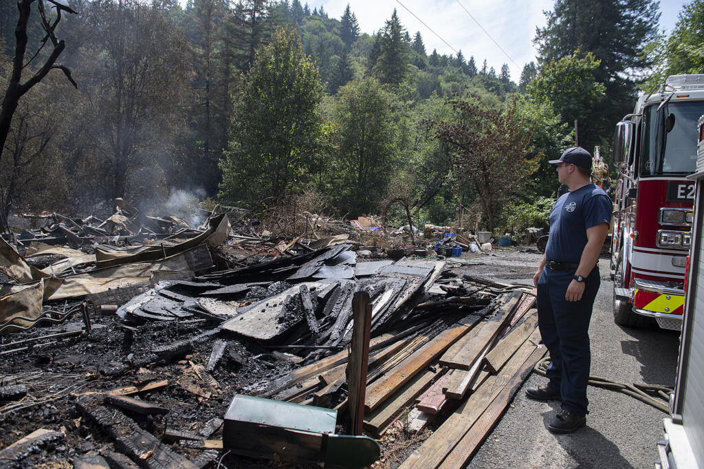 Firefighter Michael Hickey works at the scene Thursday afternoon, Aug. 17, 2023, after a blaze destroyed a primary residence and surrounding structures on the same property near La Center on Wednesday night. The incident sparked a significant brush fire that prompted evacuation warnings well into the north county community.