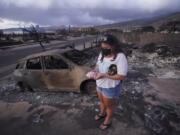 Summer Gerlingpicks up her piggy bank found in the rubble of her home following the wildfire Thursday, Aug. 10, 2023, in Lahaina, Hawaii.