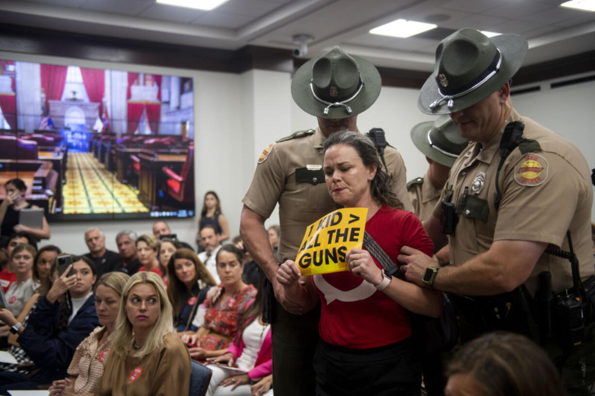 Allison Polidor is escorted out of the room by Tennessee state troopers for holding a sign reading, "1 Kid > All The Guns," during the House Higher Education Subcommittee during a special session of the state legislature on public safety, Tuesday, Aug. 22, 2023, in Nashville, Tenn.