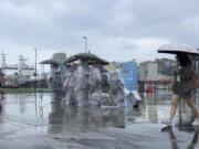 Residents with umbrellas walk past sculptures co covered up with plastic to protect from the incoming typhoon Khanun in the port city of Keelung near Taipei in northern Taiwan on Thursday, Aug. 3, 2023.