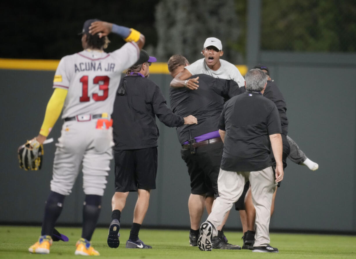 Field guards haul away one of two fans who approached Atlanta Braves right fielder Ronald Acuna Jr. (13) before the bottom of the seventh inning of a baseball game against the Colorado Rockies, Monday, Aug. 28, 2023, in Denver.