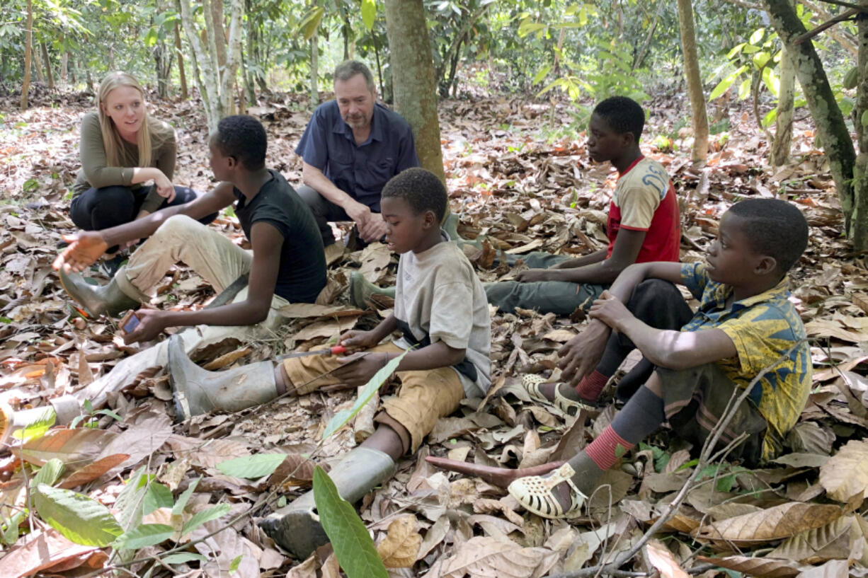 In this April, 2020 image provided by International Rights Advocates, Executive Director Terrence Collingsworth and translator Melina Cardinal Bradette, talk to children, ages 12 to 15, from Burkina Faso,  who were working on a cocoa plantation in Ivory Coast in Daloa. Child welfare advocates are suing the Biden administration for failing to block imports of cocoa picked by children in West Africa bound for America's most popular chocolate bars.