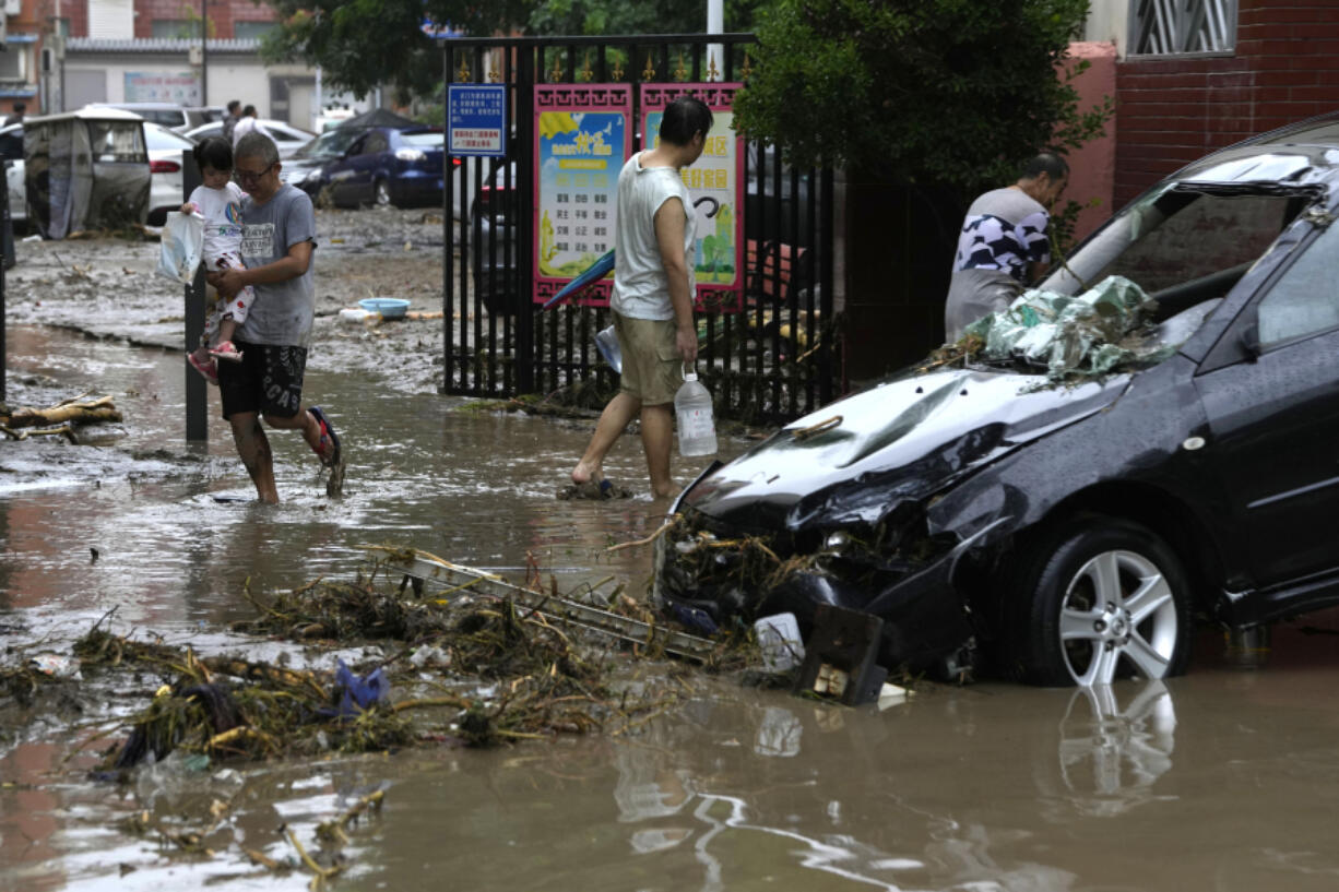 Residents walk near a vehicle damaged and left stranded by flood waters in the Mentougou district on the outskirts of Beijing, Tuesday, Aug. 1, 2023. Chinese state media report some have died and others are missing amid flooding in the mountains surrounding the capital Beijing.