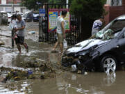 Residents walk near a vehicle damaged and left stranded by flood waters in the Mentougou district on the outskirts of Beijing, Tuesday, Aug. 1, 2023. Chinese state media report some have died and others are missing amid flooding in the mountains surrounding the capital Beijing.