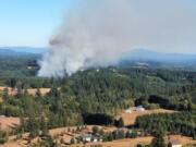 Smoke rises from a fire in a rural area near Northeast Jenny Creek Road on Wednesday afternoon. The fire began with a house fire that spread to nearby brush, prompting an evacuation of residences within a mile of the fire.