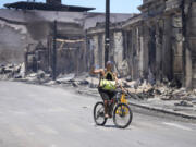 A man and dog ride along Main Street past wildfire damage on Friday in Lahaina, Hawaii.