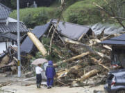 People stand by a mudslide site following a storm in Ayabe, Kyoto prefecture, western Japan Tuesday, Aug. 15, 2023. A strong tropical storm lashed central and western Japan with heavy rain and high winds Tuesday, causing flooding and power blackouts and paralyzing air and ground transportation while many people were traveling for a Buddhist holiday week.