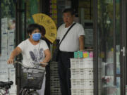 FILE - A woman pushes a bicycle past a man cooling himself with a fan at a store on a sweltering day in Beijing, July 24, 2023. Human-caused global warming made July hotter for four out of five people on Earth, according to a new report issued Wednesday, Aug. 2, 2023, by Climate Central.