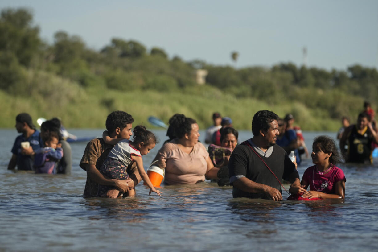 Migrants navigate around concertina wire Tuesday along the banks of the Rio Grande after crossing from Mexico into the U.S. in Eagle Pass, Texas.