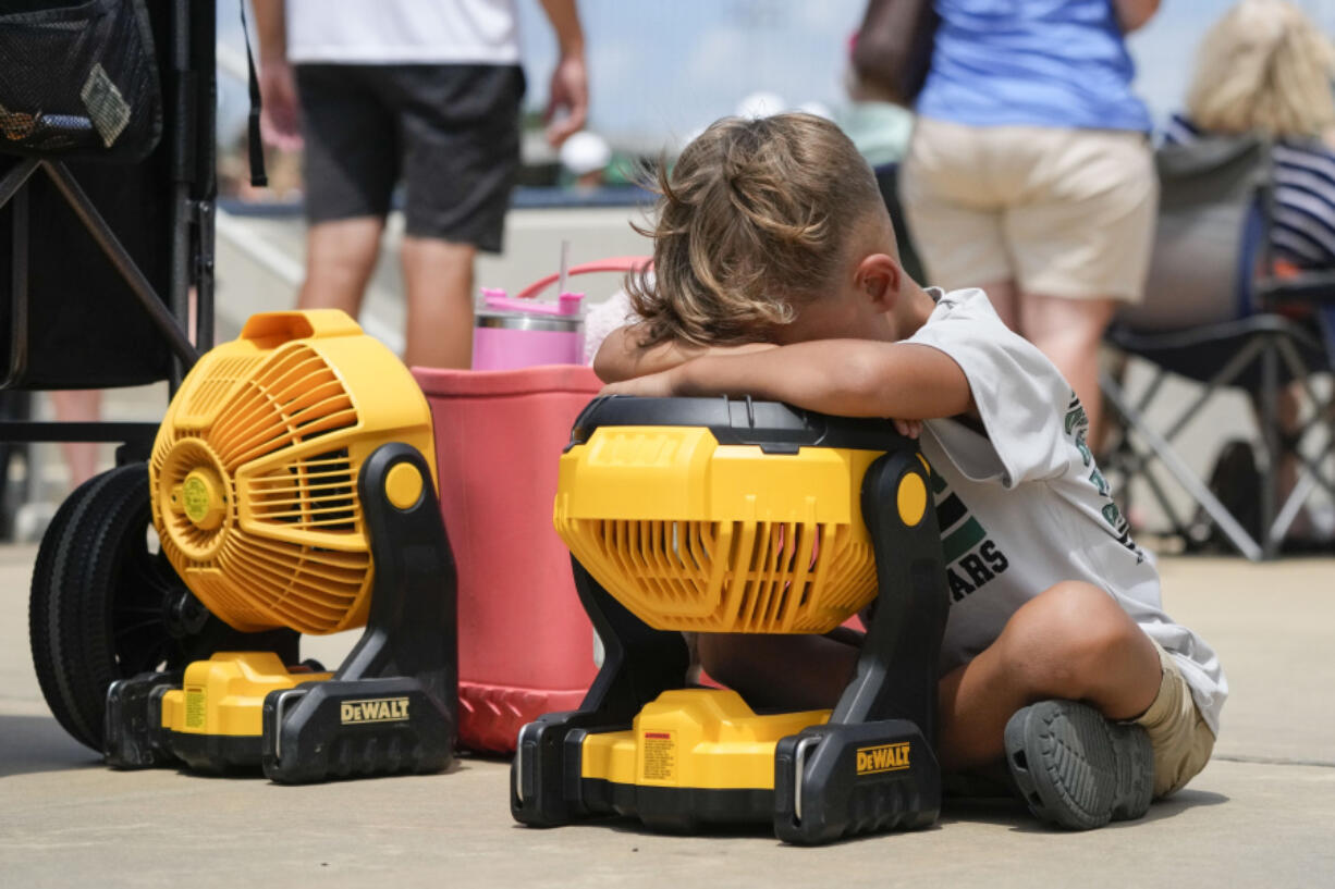 Braxton Hicks, 7, of Livingston, Texas, holds his face to a portable fan to cool off during the DYB, formerly Dixie Youth Baseball, Little League tournament in Ruston, La., Wednesday, Aug. 9, 2023. With climate change driving average global temperatures higher, organizers, players and spectators are having to pay closer attention to the heat.