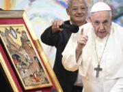 Pope Francis is helped with a microphone by Scholas Occurrentes' President Jose Maria del Corral, left, as he makes remarks about a painting depicting the parable of the 'good Samaritan' during a meeting with members of the Scholas Occurrentes community of young people, an International educational movement created by Pope Francis himself, in Cascais, 25 kilometers south of Lisbon, Thursday, Aug. 3, 2023. Francis gave the final brushstroke to the 3 km mural that the community has been working on and that is the result of the work of more than two thousand people.