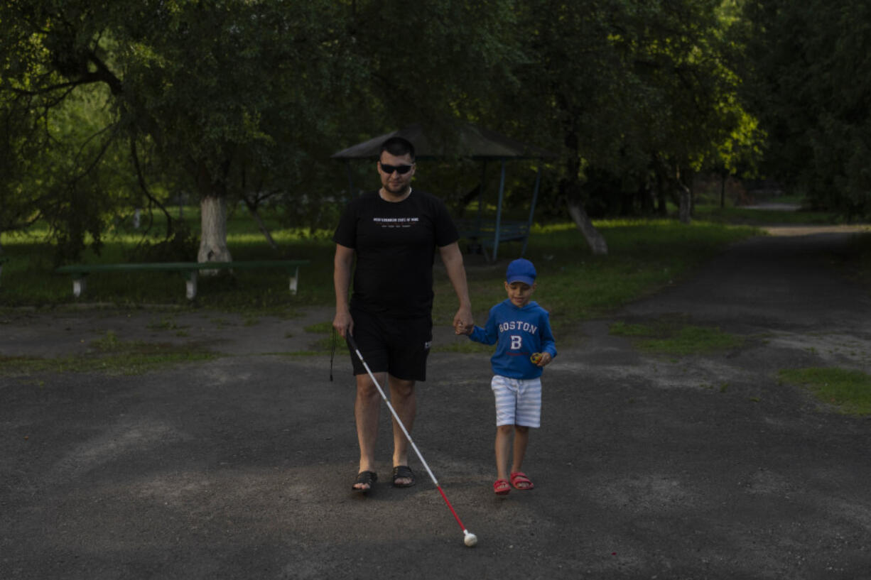 Denys Abdulin, a former Ukrainian soldier blinded in the war, walks with his son, Vadym, at a rehabilitation center designed for soldiers who lost their vision on the battlefield, near Rivne, Ukraine, Thursday, July 20, 2023. Over the course of several weeks, the veterans, accompanied by their families, reside at the rehabilitation center. Most receive their first canes here, take their first walks around urban and natural environments without assistance, and learn to operate programs on phones and computers. (AP Photo/Jae C.