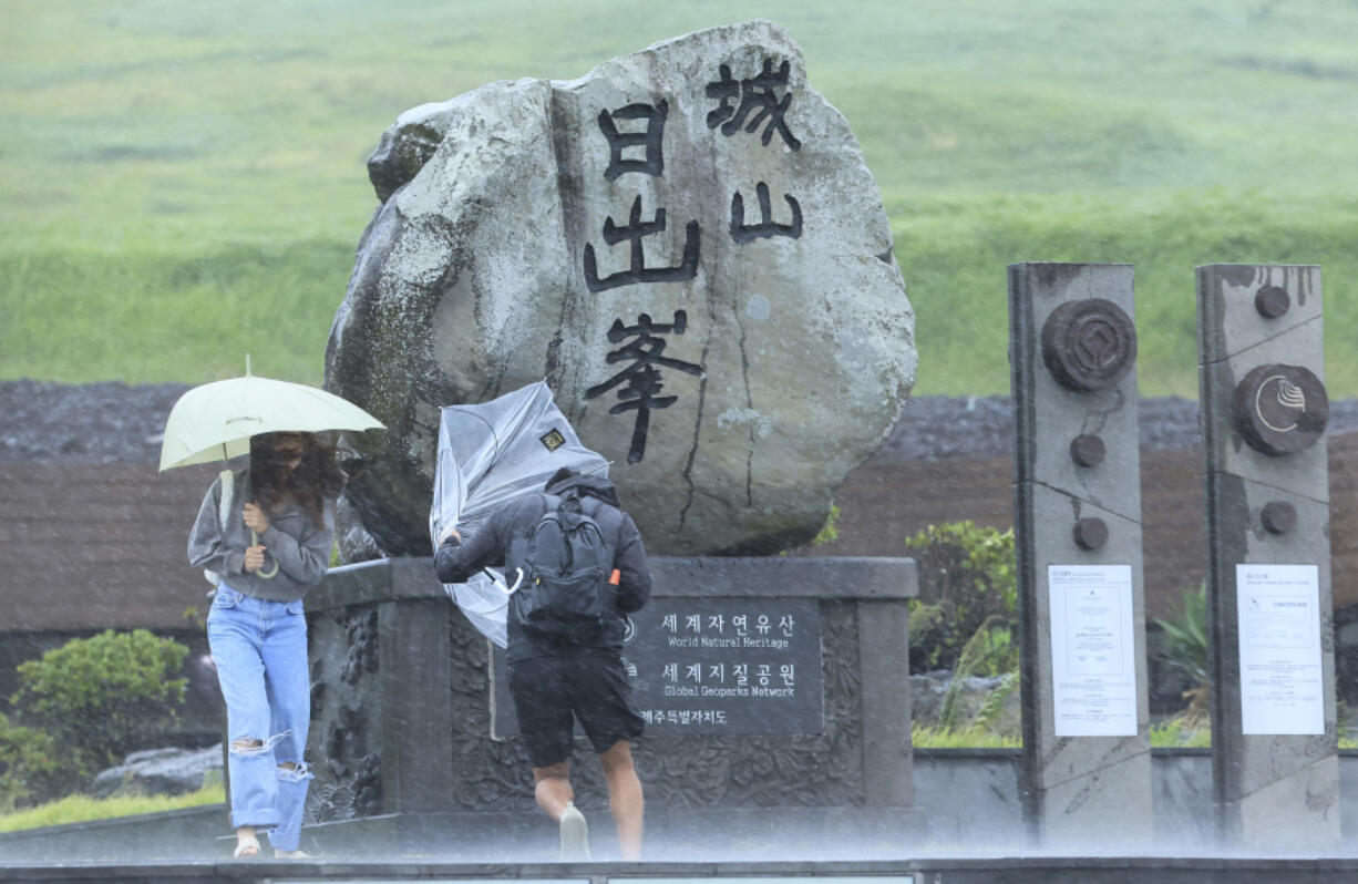 People struggle to hold onto their umbrellas in the rain and wind as the tropical storm named Khanun approaches to the Korean Peninsular, on Jeju Island, South Korea, Wednesday, Aug. 9, 2023. Dozens of flights and ferry services were grounded in South Korea on Wednesday ahead of the tropical storm that has dumped heavy rain on Japan's southwestern islands for more than a week.