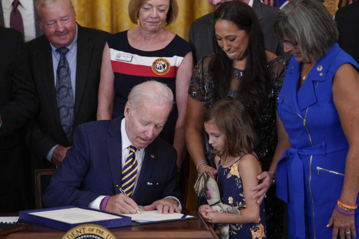 Danielle and Brielle Robinson -- the wife and daughter of Sgt. 1st Class Heath Robinson, who died of cancer two years ago -- watch as President Joe Biden signs the PACT Act on Aug. 10, 2022, in Washington.