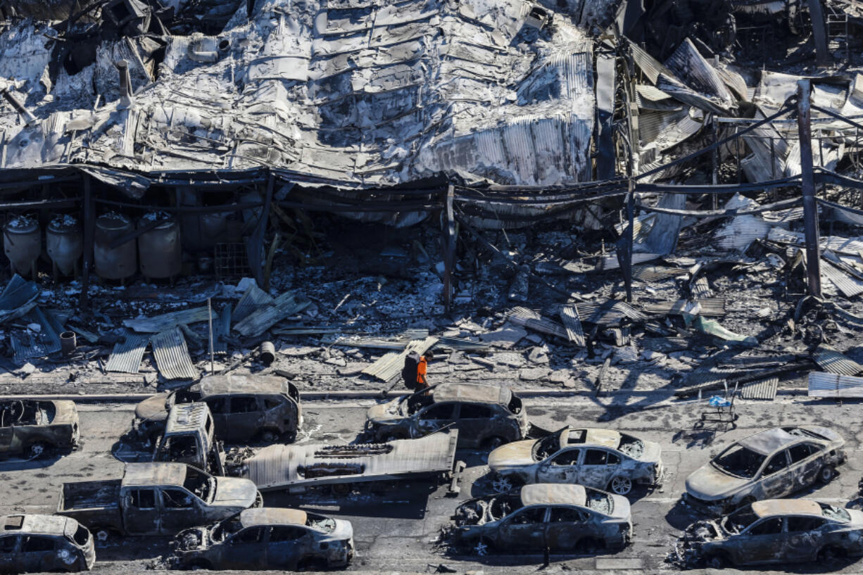 A man walks along Lahaina's Front Street on Aug. 11, 2023, past the burned carcasses of cars that couldn't escape a catastrophic wildfire that swept through the Maui, Hawaii, city.