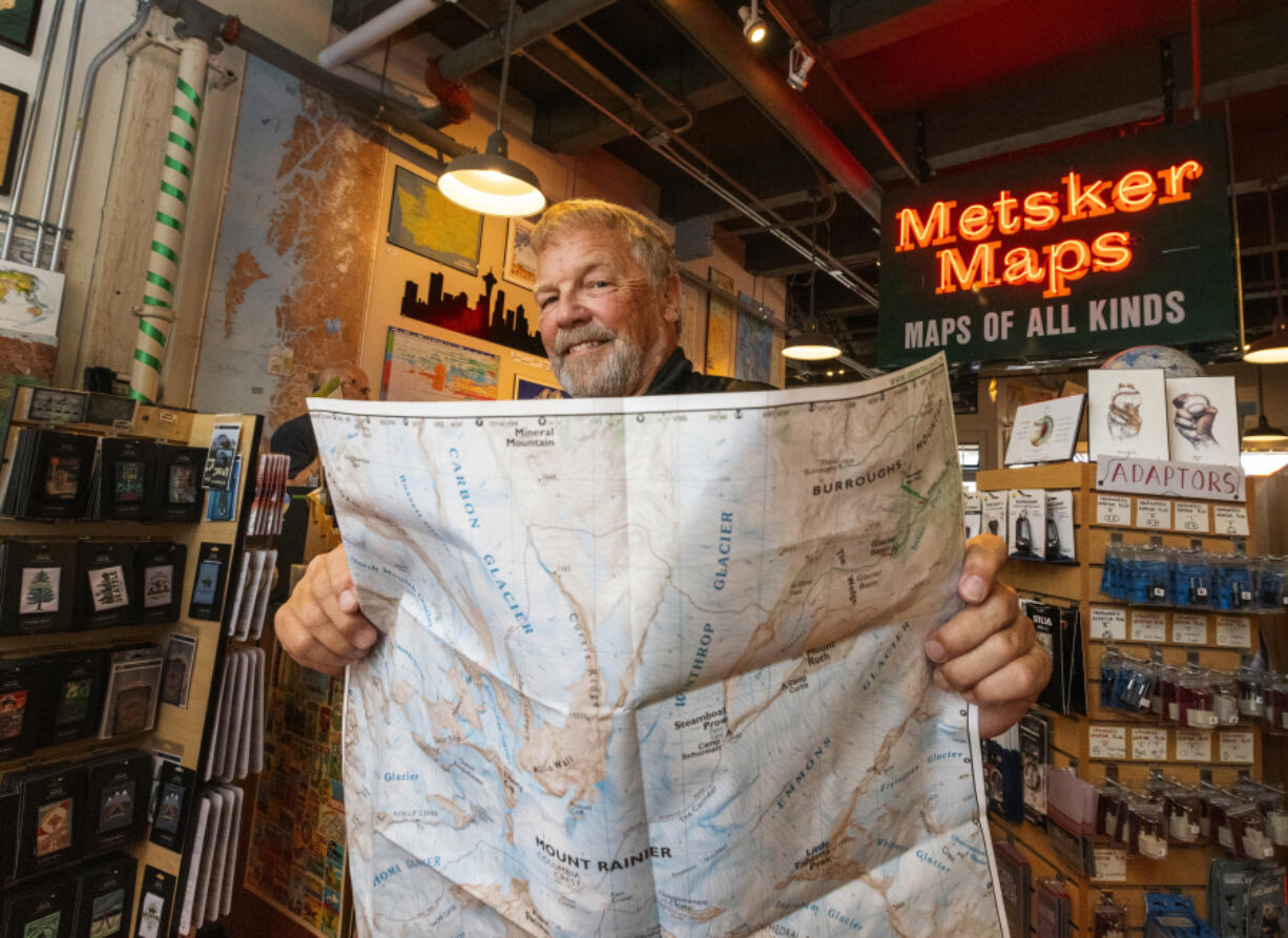 Alan Coburn, president of Green Trails Maps, holds a new revised edition of the Mount Rainier map at Metsker Maps in Seattle. The map company is turning 50 and Metsker was the first retailer to carry them.