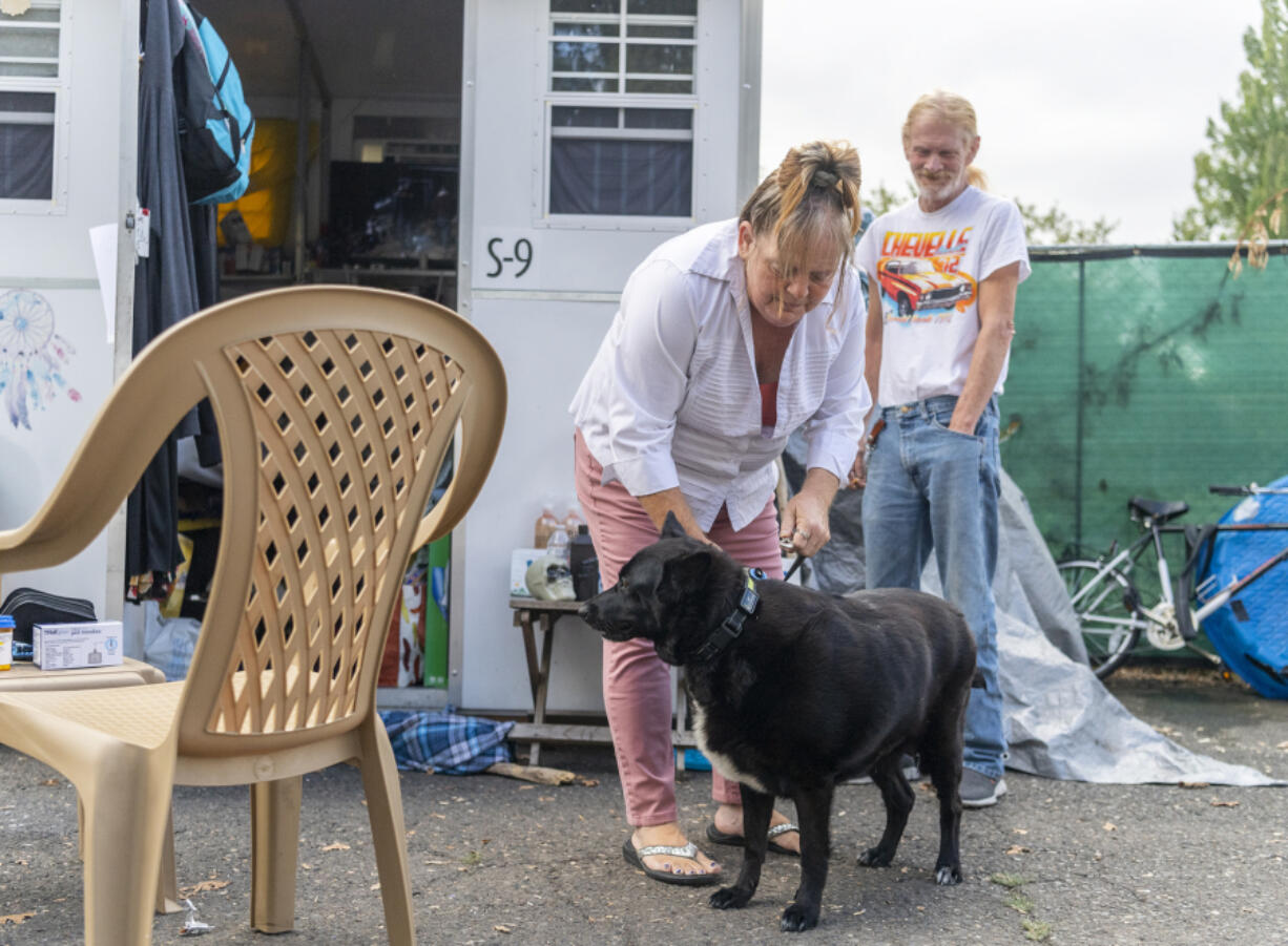 Martha Petifer, left, puts a leash on her dog, Odyssey, while her partner Clint Austin watches at The Outpost Safe Stay Community, where she has lived since February. Petifer suffered a stroke and broken back in January.