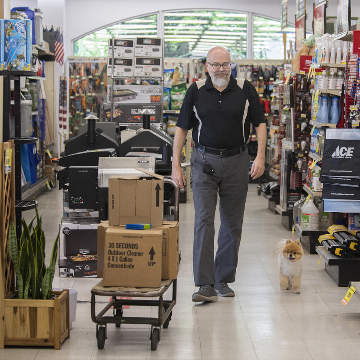 Nick Crawford, co-owner of Hi-School Hardware, walks the aisle with shop dog, Boo Boo, while working in Uptown Village.