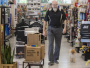 Nick Crawford, co-owner of Hi-School Hardware, walks the aisle with shop dog, Boo Boo, while working in Uptown Village.