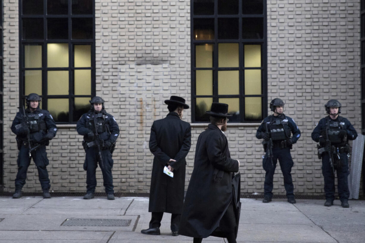 Orthodox Jewish men pass New York City police guarding a Brooklyn synagogue on Dec. 11, 2019, prior to a funeral for Mosche Deutsch, a rabbinical student from Brooklyn who was killed in a shooting at a Jersey City, N.J., market. Ahead of the High Holidays, encompassing Rosh Hashana and Yom Kippur, that began this week, a network of Jewish security experts and religious leaders hosted several webinars to help prepare for the season.