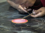 Tibetan Buddhist monk Nawang Shakga works on a sand mandala Monday at Clark College's Cannell Library. The mandala's creation began with the outline of a small orange circle at the very center, which was then filled with a soft pink.