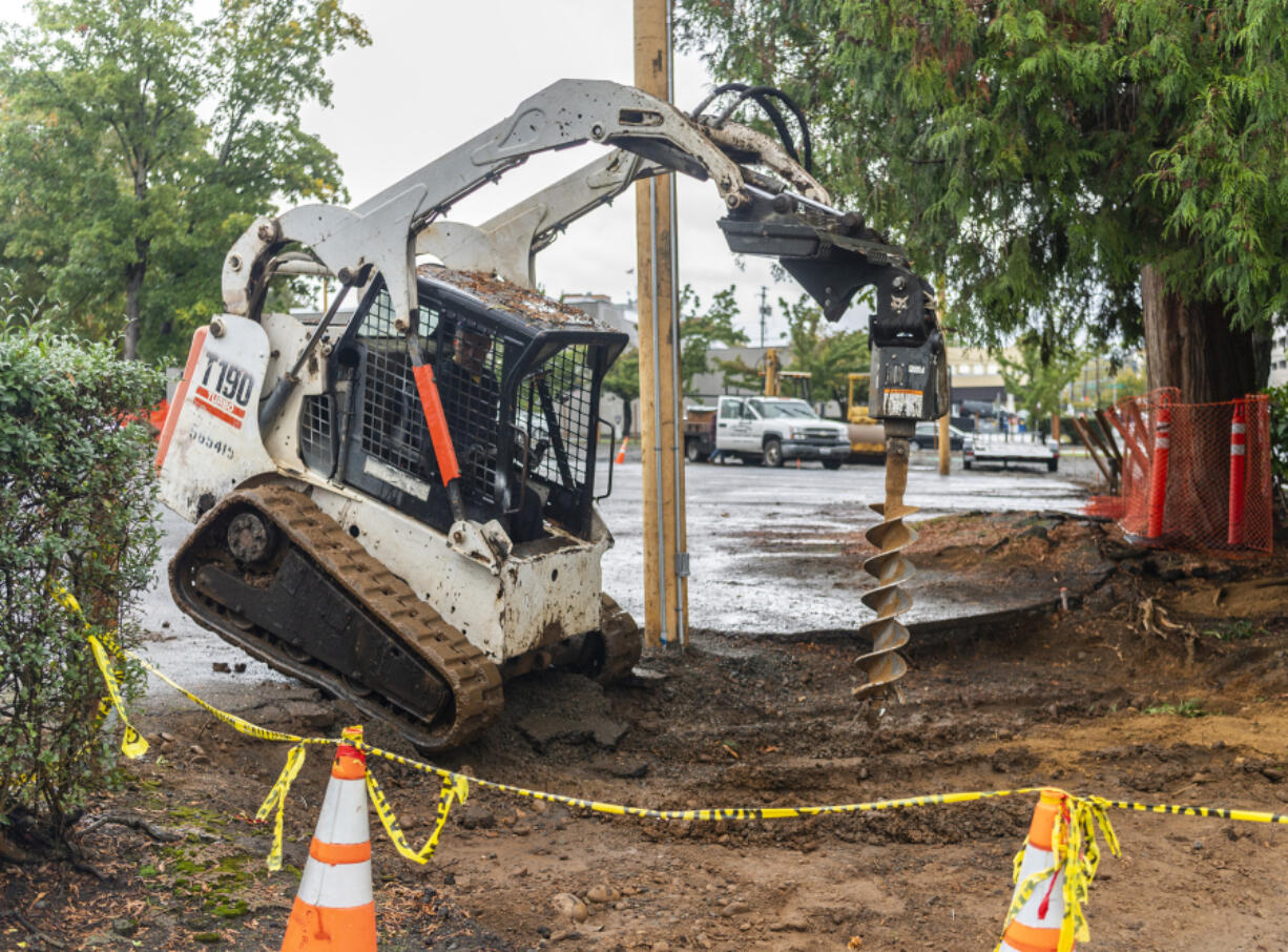 A worker with Unlimited Fence repositions a fence post hole drilling machine Monday on West 11th Street.