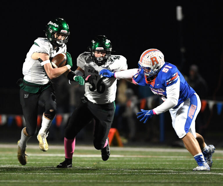 Woodland junior Elijah Andersen, left, runs with the ball while junior Charles Elkinton, center, blocks Ridgefield senior Mason Curran on Friday, Oct, 27, 2023, during the Beavers’ 28-21 win against Ridgefield at Ridgefield High School. With the win, Woodland captured its first 2A Greater St. Helens League title since 2007.