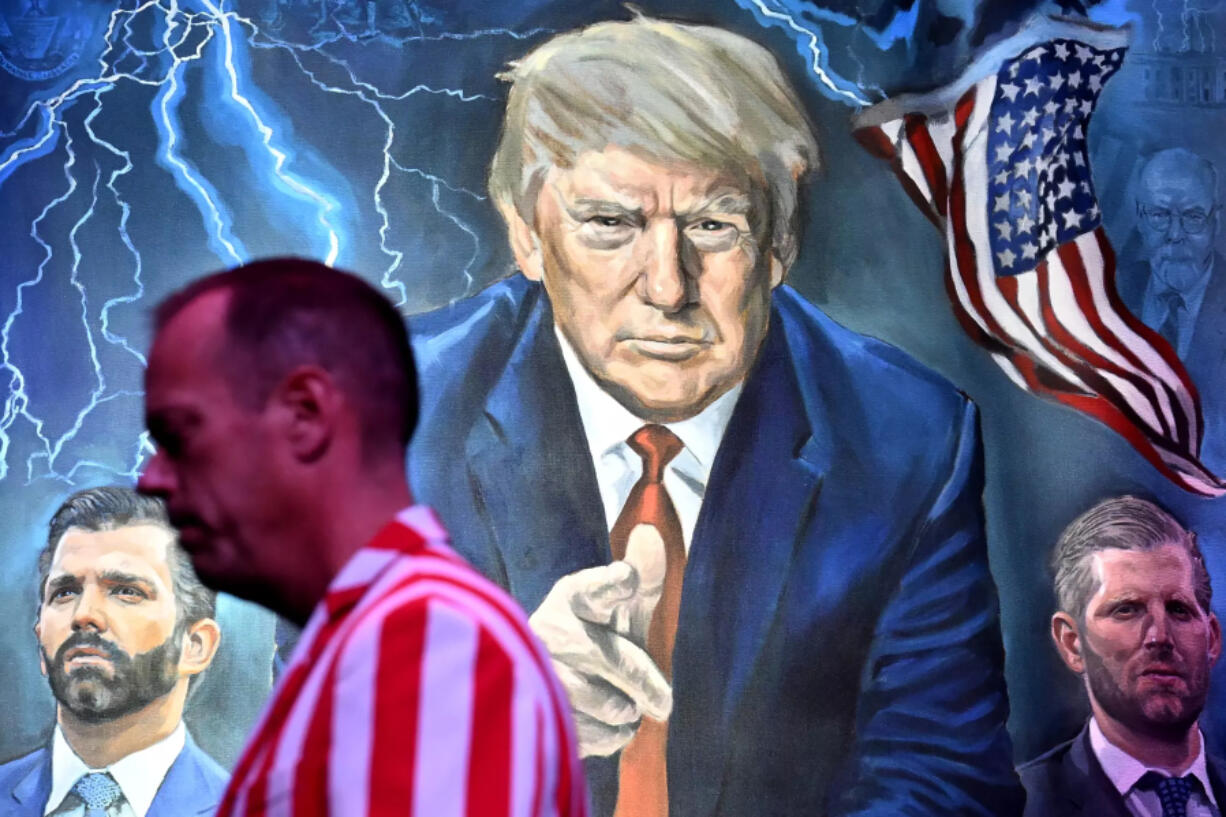 A stage crew member walks by a poster of former President Trump and his sons Don Jr. and Eric during the ReAwaken America Tour in North Las Vegas.