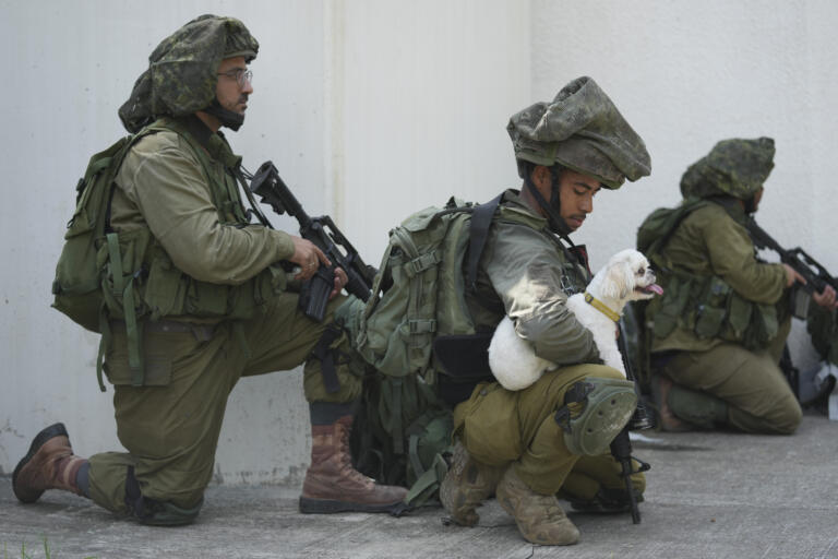 An Israeli soldier holds a dog in kibbutz Kfar Azza on Tuesday, Oct. 10, 2023. Hamas militants overran Kfar Azza on Saturday, where many Israelis were killed and taken captive.