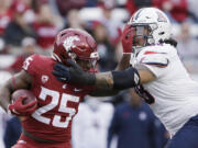 Washington State running back Nakia Watson (25) carries the ball while pressured by Arizona defensive lineman Tiaoalii Savea during the first half of an NCAA college football game Saturday, Oct. 14, 2023, in Pullman, Wash.