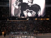 The Pittsburgh Penguins and Anaheim Ducks gather at center ice, before an NHL hockey game in Pittsburgh, Monday, Oct. 30, 2023, to honor former Penguin player Adam Johnson, shown on the scoreboard, who died in a "freak accident" while playing in an English hockey league game. (AP Photo/Gene J.